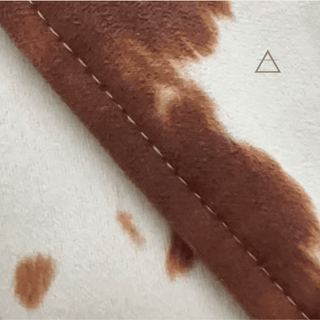 Gros plan du tissu imprimé effet peau de vache brun et ivoire du blazer Bérénice, avec une couture visible.