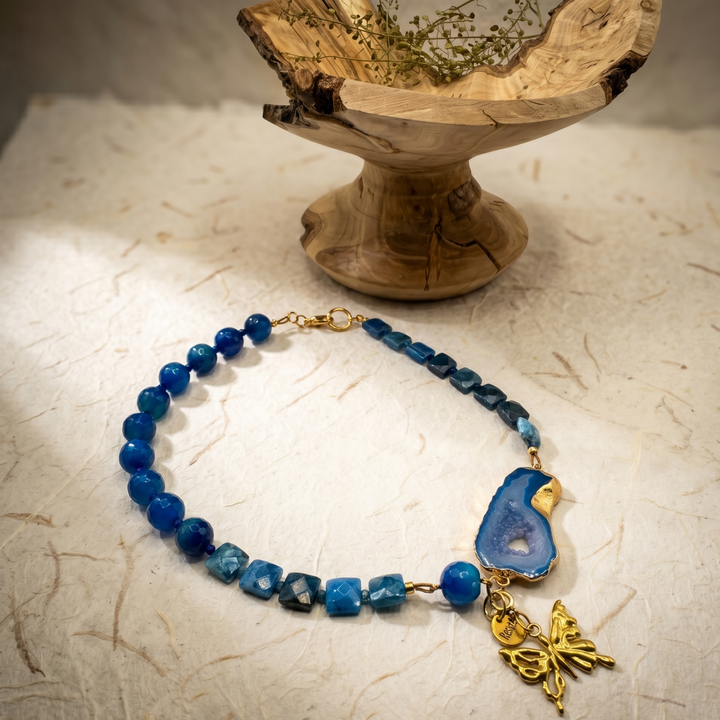 Collier Blue Portal aux perles bleues, avec une tranche d’agate au contour doré et un charm papillon.