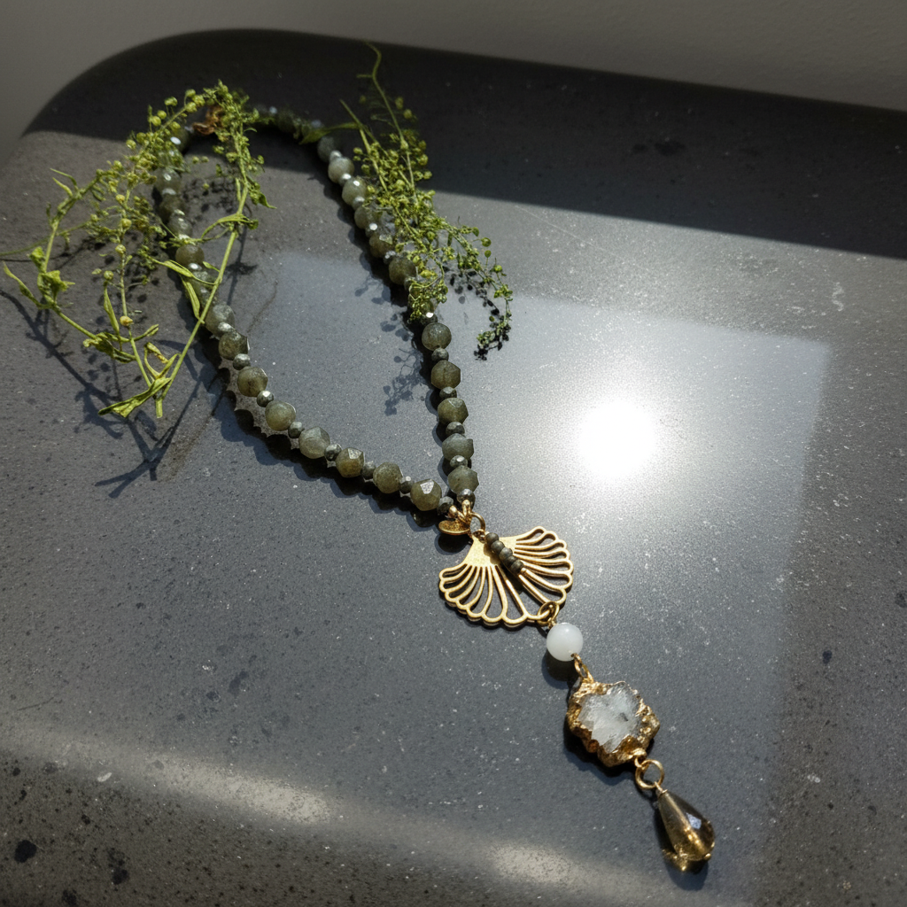 Collier Labradorite Moonlight aux perles gris fumé, avec éléments dorés et pendentif en quartz, présenté sur un fond sombre avec des tiges végétales.
