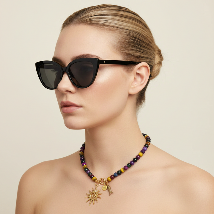 Collier SOLSTICE porté sur peau nue, avec perles multicolores et pendentifs soleil et poisson dorés.