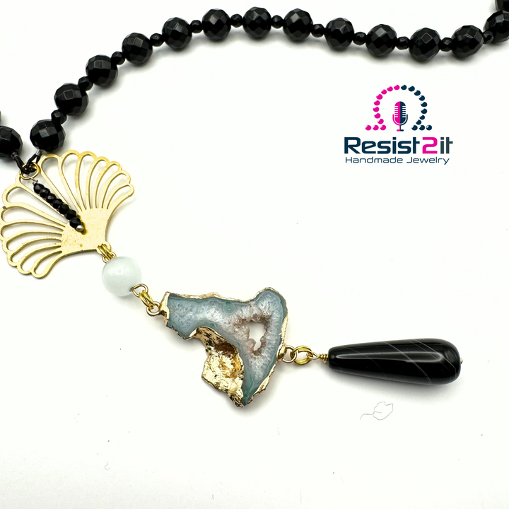 Détail du pendentif Ocean Midnight, avec élément ajouré doré, perle blanche, pierre bleu pâle et goutte noire.