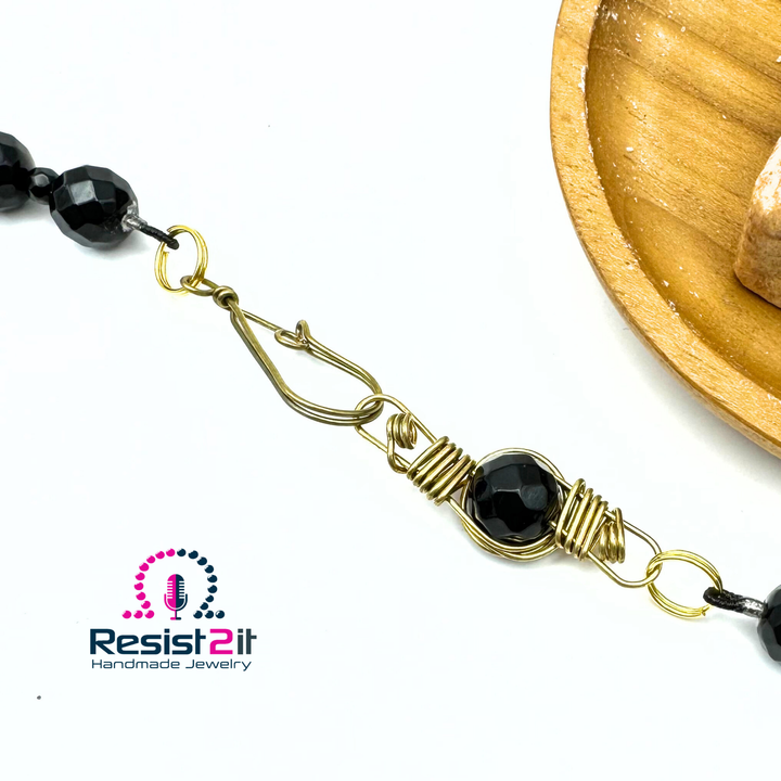 Détail du fermoir à crochet doré du collier Ocean Midnight, avec perle noire entourée de fil.