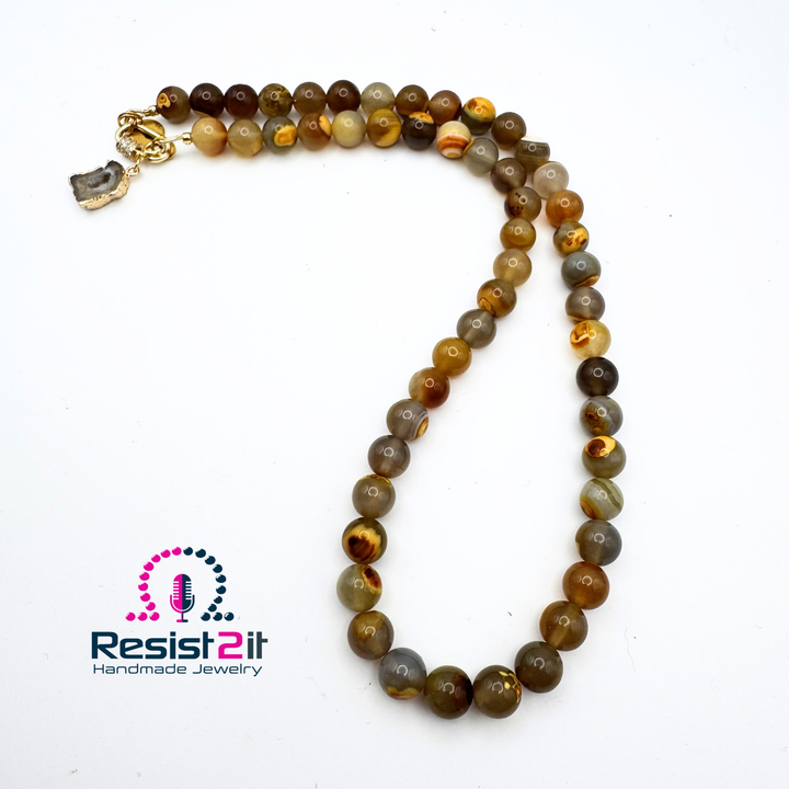 Collier Unspoken disposé en boucle sur fond blanc, avec ses perles aux nuances de brun, de miel et de gris.