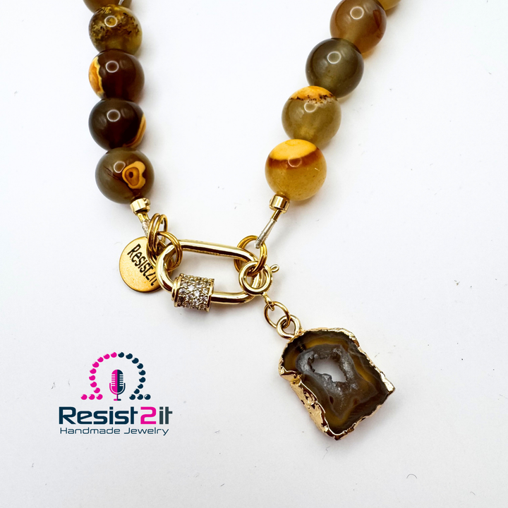Détail du fermoir de teinte dorée du collier Unspoken et de son pendentif en tranche d’agate.