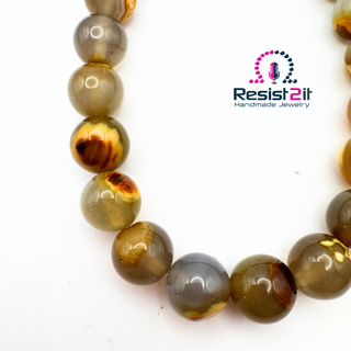 Gros plan des perles du collier Unspoken, aux motifs bruns et miel sur un fond gris translucide.