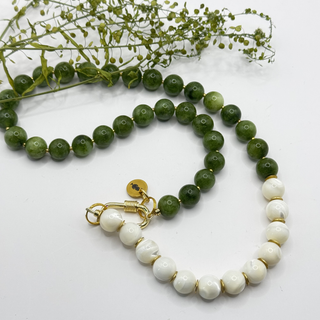 Collier Midnight Reflections aux perles vertes nuancées et blanches, avec fermoir ovale doré, disposé en courbes sur fond clair.